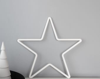 May include: A white, five-pointed star-shaped wall decoration. The star is made of a continuous line and is set against a gray background. A white decorative tree is on the left side of the star.