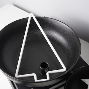 May include: A black, round candle holder with a white, geometric tree-shaped design. The candle holder has a small, black cylindrical base for the candle. The design is modern and minimalist.