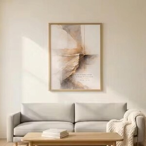 Pode incluir: Uma impressão de arte abstrata emoldurada com uma paleta de cores neutras está pendurada acima de um sofá cinza claro. A obra de arte apresenta um design em estilo aquarela em tons de bege e marrom. Uma mesa de centro de madeira e um cobertor creme completam a sala de estar.