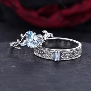 May include: A silver-toned ring set featuring a pear-cut light blue gemstone on a band with leaf-shaped metalwork and small accent stones. The second band is a silver-toned ring with an engraved leaf pattern and a single rectangular light blue stone.
