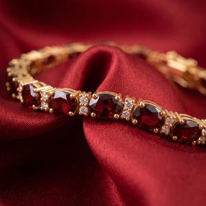 Könnte beinhalten: Ein goldfarbenes Armband mit einer Reihe von oval geschliffenen, tiefroten Granat-Edelsteinen, die sich mit kleinen, klaren, rund geschliffenen weißen Akzentsteinen abwechseln. Metallglieder verbinden die Fassungen zu einer Kette.