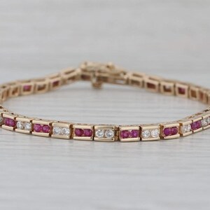 Könnte beinhalten: Ein Tennisarmband aus Roségold mit einem abwechselnden Muster aus rund geschliffenen, leuchtend roten Rubinen und klaren weißen Diamanten, die in einen kanalartigen Metallrahmen gefasst sind. Das Armband hat einen sicheren Kastenschlossverschluss.