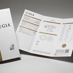 May include: A GIA Diamond Grading Report and accompanying booklet. The booklet is white with gold trim and the GIA logo. The report is open, displaying diamond diagrams and data. The background is a gradient of gray.