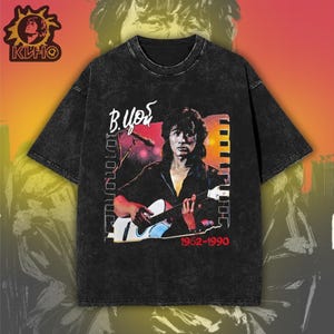 May include: A black acid-wash t-shirt featuring a graphic print of a musician playing an acoustic guitar. The design includes the Cyrillic text "В. Цой" and the years "1962-1990" in red. A circular logo with the text "КИНО" is in the top left corner.