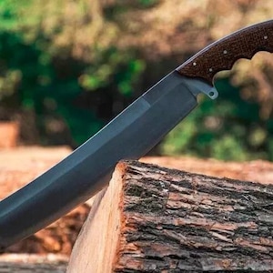 May include: A large, dark-bladed knife with a brown, textured handle. The blade is angled and rests on a piece of wood. The handle has a curved design for grip. The knife appears to be a tool for cutting or chopping.