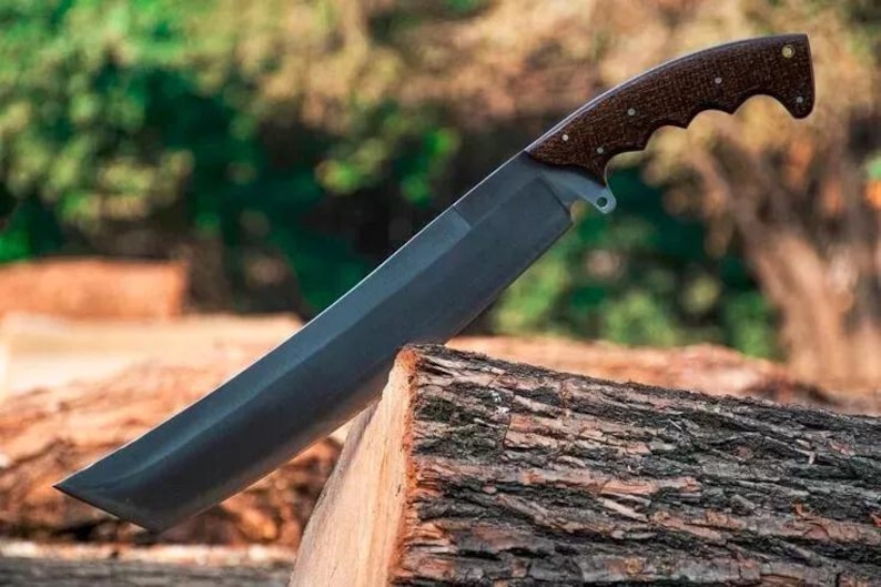 May include: A large, dark-bladed knife with a brown, textured handle. The blade is angled and rests on a piece of wood. The handle has a curved design for grip. The knife appears to be a tool for cutting or chopping.