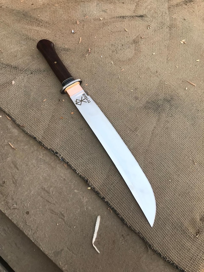 May include: A long, silver blade knife with a dark brown wooden handle. The blade has the word "Mimir" etched on it. The knife is lying on a brown, textured surface.