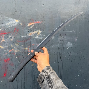 May include: A black sword with a curved blade. The handle is dark with white accents. The sword is held against a dark grey background with colourful paint splatters.