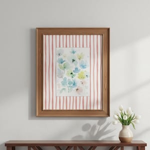 May include: A framed watercolor floral print with a wooden frame. The artwork features blue, green, and pink flowers on a white background. The frame has a pink and white striped border. A vase of white tulips sits on a wooden table.