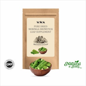 Może przedstawiać: Brązowa papierowa torba z kremową etykietą z napisem: "PURE DRIED MORINGA DRUMSTICK LEAF SUPPLEMENT". Drewniana miska zawiera zielone pałeczki moringa. Widoczne jest również logo "Natural n Tasty".