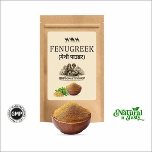 Pode incluir: Uma bolsa de papel castanho rotulada FENUGREEK com um gráfico de camelos, um casal e uma taça de pó. Uma taça de madeira cheia de pó de feno-grego castanho está à frente. Um logótipo GMP e o texto Natural n Tasty são visíveis na imagem.