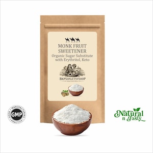 Op de afbeelding: Een bruine papieren zak met het opschrift "MONK FRUIT SWEETENER". Daaronder een houten kom gevuld met wit poeder. De tekst op het etiket luidt ook "Organic Sugar Substitute with Erythritol, Keto". Het logo "Natural n Tasty" is ook zichtbaar.