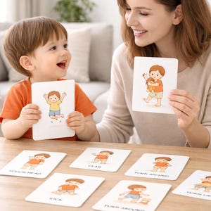 Peut inclure: Un enfant et un adulte tiennent des cartes illustr&eacute;es avec des dessins d'un enfant de dessin anim&eacute; effectuant des actions. Les cartes sont sur une table en bois. Les cartes comportent des textes tels que "Toucher la t&ecirc;te" et "Donner un coup de pied".