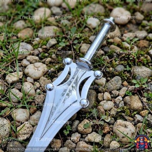 May include: A silver-colored metal dagger featuring a pointed blade with a central ridge, a crossguard with four rounded decorative spheres, and a cylindrical handle. The surface of the metal is reflective and smooth, showing a metallic finish.