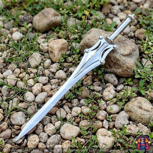 May include: A silver-colored metal dagger featuring a pointed blade and a decorative hilt with four rounded studs. The handle is cylindrical and smooth, leading to a symmetrical guard that tapers into a sharp, straight blade with a polished finish.