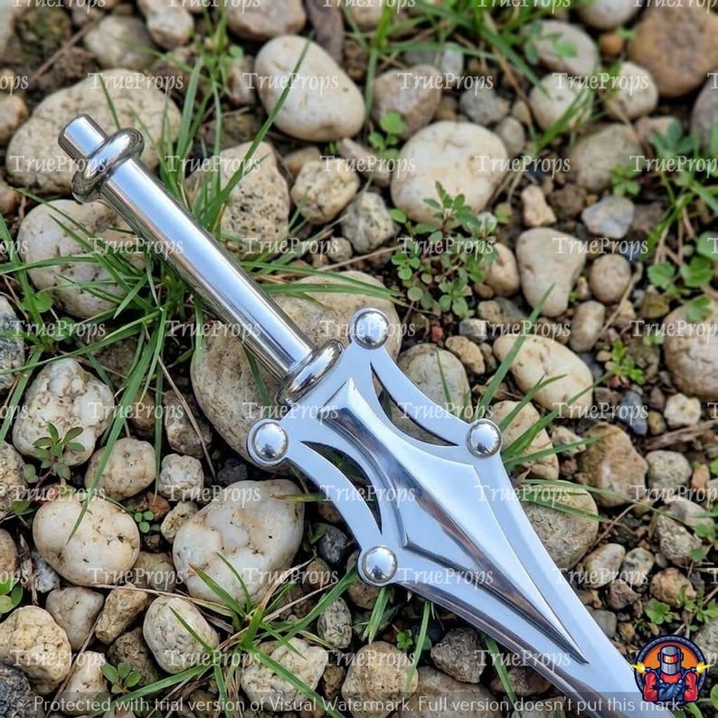 May include: A silver-toned metal dagger featuring a cylindrical handle with a rounded pommel and a pointed blade. The guard has a symmetrical, open-work design with four small, spherical accents at the corners. The surface is reflective.