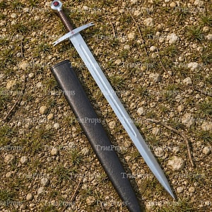 May include: A silver-toned steel sword with a brown leather-wrapped grip and a circular pommel featuring a red cross emblem. The crossguard displays small red cross symbols on each end. A black scabbard lies alongside the blade on the ground.