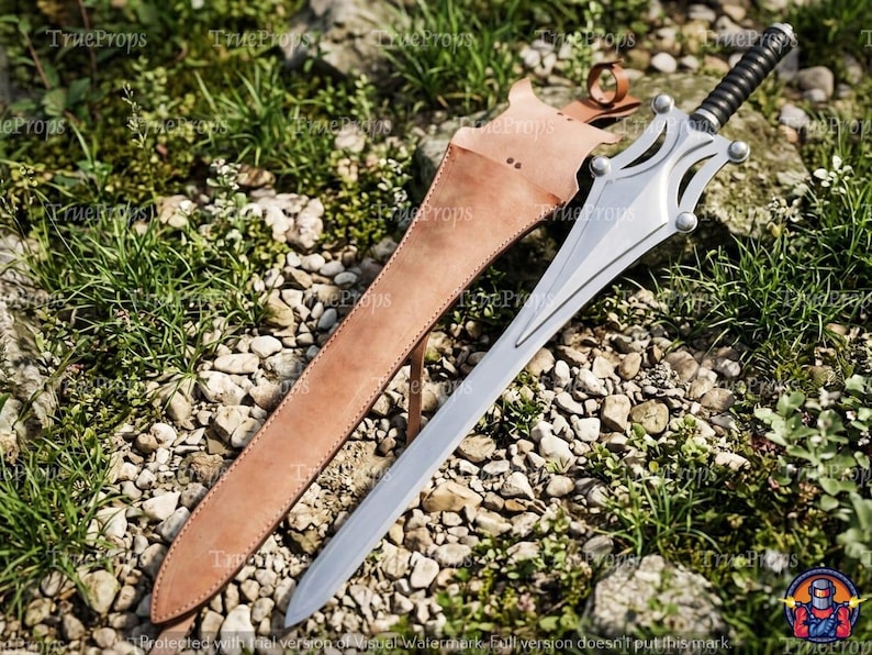 Puede incluir: Una espada de metal plateado con hoja puntiaguda y empu&ntilde;adura negra acanalada, que presenta una guarda decorativa con cuatro detalles circulares. La espada se acompa&ntilde;a de una funda de cuero color canela con correa y hebilla.