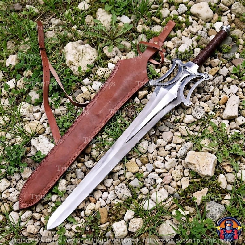 Puede incluir: Una espada de acero de doble filo con una compleja guarda de metal calado y un mango envuelto en color marr&oacute;n oscuro. La espada viene acompa&ntilde;ada de una funda de cuero marr&oacute;n a juego con una correa ajustable integrada para llevarla.