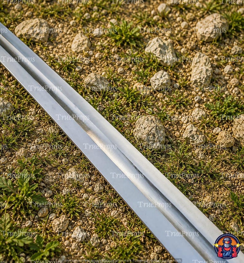 May include: A long, straight, double-edged metal sword blade with a central fuller running down the length of the steel. The blade features a polished, reflective surface that tapers toward a sharp point, showcasing a clean, metallic finish.