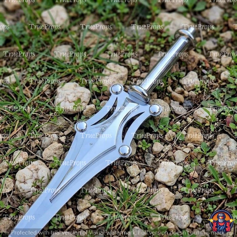 May include: A silver-colored metal dagger featuring a pointed blade and a decorative hilt with four circular rivets. The handle is cylindrical with a rounded pommel. The surface of the metal is reflective and smooth, showing a metallic finish.