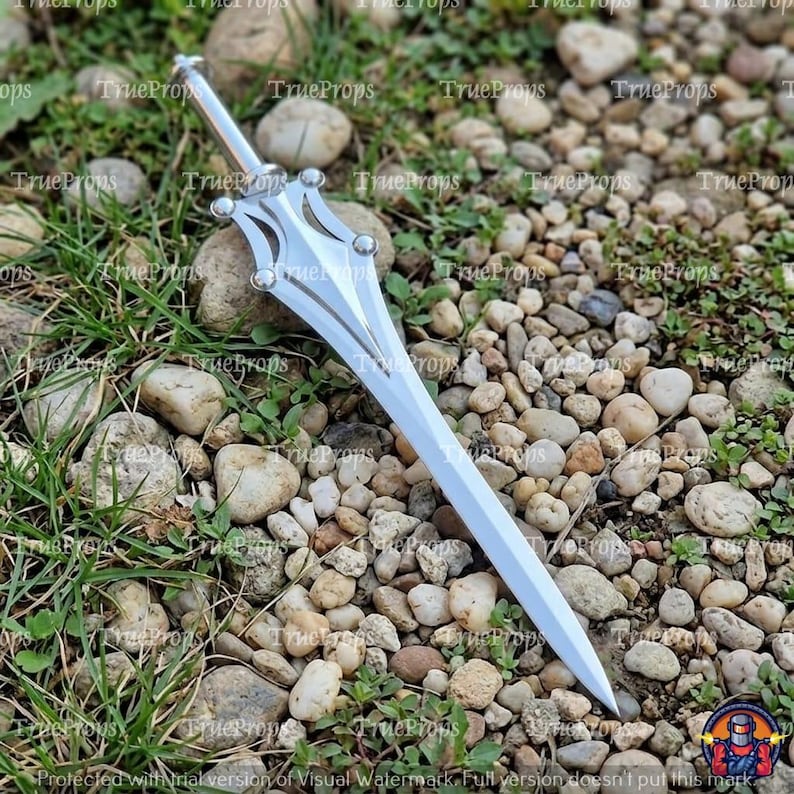May include: A silver-colored metal dagger featuring a pointed blade and a decorative crossguard with four rounded accents. The handle is cylindrical and leads to a pommel, with the entire object displaying a polished, reflective finish.