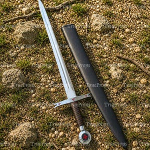 May include: A silver-toned metal sword with a double-edged blade and a central fuller. The crossguard features red cross emblems, and the handle is wrapped in dark brown material. A matching black scabbard lies beside the sword on the ground.