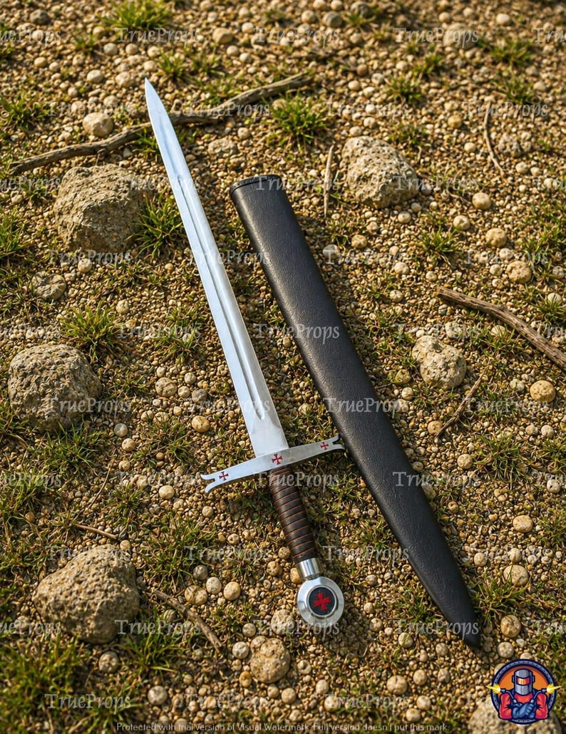 May include: A silver-toned metal sword with a double-edged blade and a central fuller. The crossguard features red cross emblems, and the handle is wrapped in dark brown material. A matching black scabbard lies beside the sword on the ground.