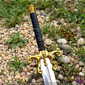 Puede incluir: Una espada con hoja de plata pulida, empu&ntilde;adura envuelta en negro y una guarda de color dorado con un peque&ntilde;o detalle de calavera en el centro. El pomo es una tapa sencilla de color dorado y la guarda tiene extremos curvos y ornamentados.