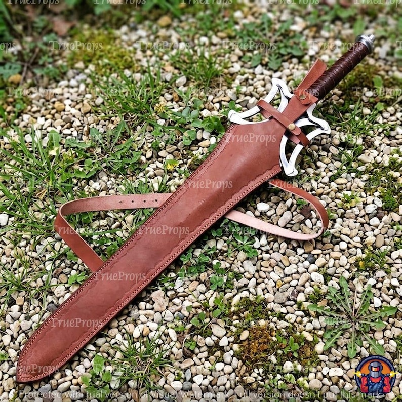 Puede incluir: Una espada con empu&ntilde;adura envuelta en cuero marr&oacute;n oscuro y una guarda de metal plateado con un dise&ntilde;o calado intrincado. La hoja est&aacute; enfundada en una vaina de cuero marr&oacute;n a juego con una correa de cuero larga y ajustable.