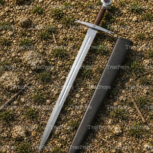 May include: A silver-toned metal sword with a double-edged blade and a central fuller. The hilt features a brown leather-wrapped grip, a crossguard with small red cross emblems, and a circular pommel with a red cross detail, accompanied by a black scabbard.