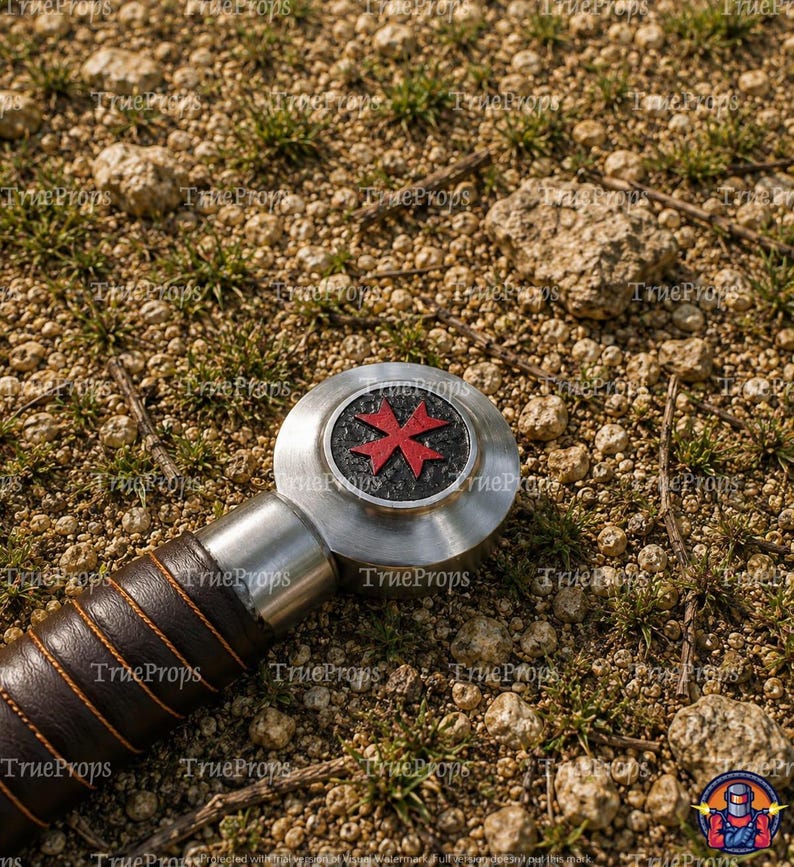 May include: A sword pommel featuring a circular silver metal design with a textured black center and a red Maltese cross emblem. The handle is wrapped in dark brown leather with visible orange stitching, showing a metallic finish.