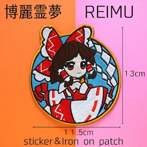 以下が含まれることがあります： 赤と白の衣装と茶色の髪の漫画のキャラクターが描かれた、円形のステッカーとアイロン接着パッチ。パッチは幅11.5cm、高さ13cmです。「REIMU」という文字が右側にあり、他の文字は日本語です。