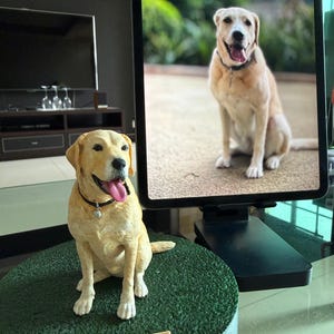 May include: A custom-made yellow Labrador retriever figurine sitting on a circular green textured base. The dog sculpture features a black collar with a small charm and a nameplate that reads Whiskey in raised white lettering.