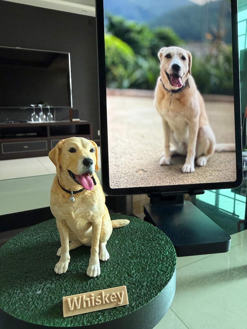 May include: A custom-made yellow Labrador retriever figurine sitting on a circular green textured base. The dog sculpture features a black collar with a small charm and a nameplate that reads Whiskey in raised white lettering.