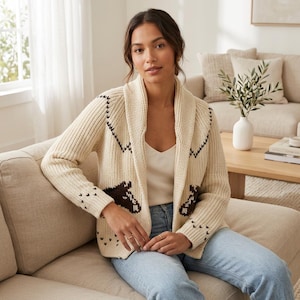 Pode incluir: Um cardigã de malha na cor creme com gola xale e um padrão de cabeça de cavalo marrom escuro no peito e nas mangas. O suéter tem uma textura canelada, mangas compridas e um design frontal aberto, combinado com calças jeans azul claro.