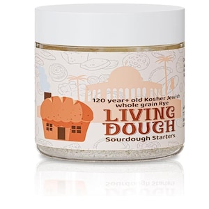 May include: A clear glass jar with a white lid, filled with a light-coloured powder. The jar features a label with the text "120 year+ old Kosher Jewish whole grain Rye LIVING DOUGH Sourdough Starters" and a cartoon illustration of a bread house.