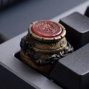 May include: A white ceramic mug with a black handle and the text "But First, Coffee" in a handwritten style. The mug is on a white surface. The mug is approximately 10 cm tall.