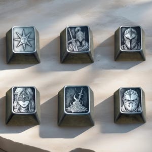 May include: Six metallic keycaps with engraved designs. The keycaps feature images of a sun, a knight with a sword, a knight's helmet, a woman with a mask, a bonfire with a sword, and a knight's helmet. The keycaps are a muted bronze colour.
