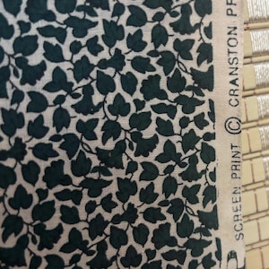 May include: Close-up of fabric with a repeating pattern of dark green ivy leaves on a white background. The fabric has a natural, slightly textured appearance. The words "SCREEN PRINT" and "CRANSTON PRINT WORKS" are visible.