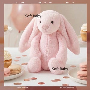 May include: A cuddly pink bunny rabbit toy with long, drooping ears. The toy is made of soft material and is sitting up. The words "Soft Baby" are printed on the image. The background features cupcakes, macarons, and a balloon.