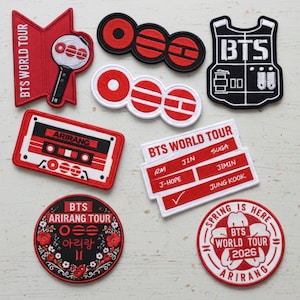 May include: A collection of embroidered patches in red, black, and white. Designs include the text "BTS WORLD TOUR", a cassette tape, a vest, and various circular and rectangular shapes. Some patches feature the names of band members.