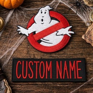 May include: A circular embroidered patch featuring a white ghost character inside a red circle with a diagonal slash, positioned above a rectangular black embroidered patch with the red text CUSTOM NAME stitched in a bold, sans-serif font.