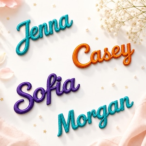 May include: Four embroidered name patches in cursive script. The names Jenna and Morgan are in teal, Casey is in orange, and Sofia is in purple. Each patch features a raised, stitched border and a soft, fabric-like texture for personalized items.