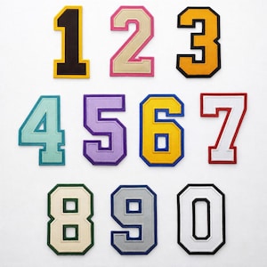 May include: A collection of embroidered number patches in various colors, including black, pink, yellow, teal, purple, and white. Each number has a contrasting border, creating a bold, collegiate style.