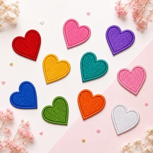 May include: A collection of ten heart-shaped embroidered patches in various solid colors including red, pink, purple, yellow, teal, blue, green, orange, and white. Each patch features a stitched border and a textured fabric surface.