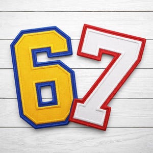 May include: Embroidered patches featuring the numbers 6 and 7. The number 6 is yellow with a blue outline, while the number 7 is white with a red outline. The patches are likely for sports jerseys or apparel.