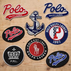 May include: A collection of embroidered patches featuring the "Polo Ralph Lauren" logo in various designs. The patches include the word "Polo" in script, an anchor, a crown, and a polo player. Colors include red, white, blue, and black.