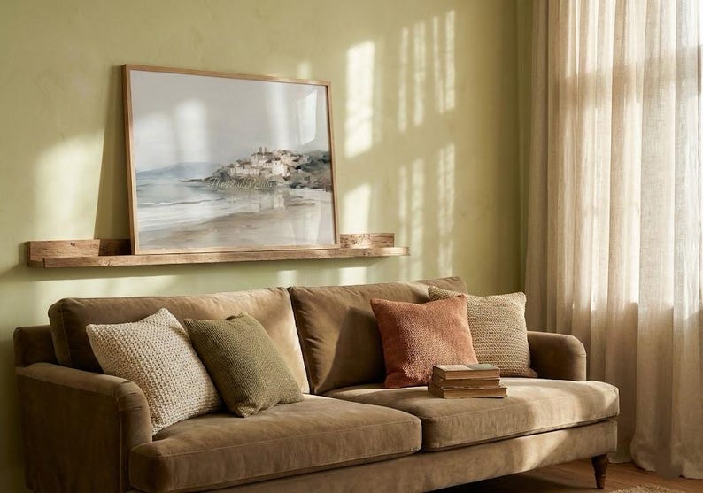Puede incluir: Sal&oacute;n con un sof&aacute; marr&oacute;n y cojines en tonos beige, verde y naranja. Un cuadro enmarcado con un paisaje cuelga sobre el sof&aacute;, sobre una estanter&iacute;a de madera. La habitaci&oacute;n tiene una paleta de colores neutros.