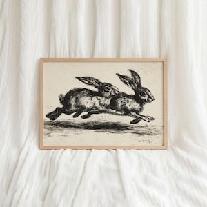 Puede incluir: Una impresión en blanco y negro enmarcada que representa dos conejos corriendo. La obra de arte tiene una estética vintage, con representaciones detalladas de los conejos. El marco es de madera clara.
